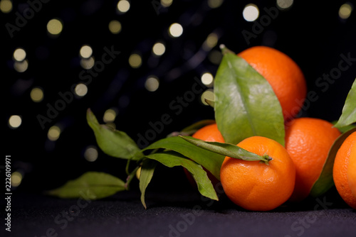 Fresh Clementines or Tangerines with Xmas Lights on the background. Whole ripe tangerines with green young leaves on a dark background. Christmas concept.