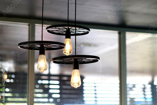 Glowing vintage light bulb with warm golden illumination, Industrial style ceiling pendant lights with black metal wheel frames, glowing bulbs, warm vintage for cafe, restaurant and home interiors