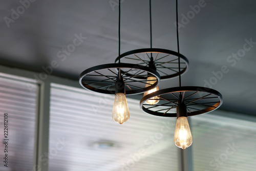 Glowing vintage light bulb with warm golden illumination, Industrial style ceiling pendant lights with black metal wheel frames, glowing bulbs, warm vintage for cafe, restaurant and home interiors