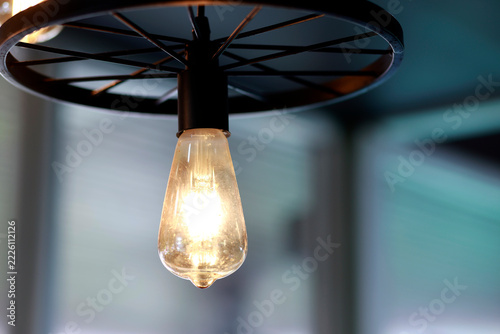 Glowing vintage light bulb with warm golden illumination, Industrial style ceiling pendant lights with black metal wheel frames, glowing bulbs, warm vintage for cafe, restaurant and home interiors