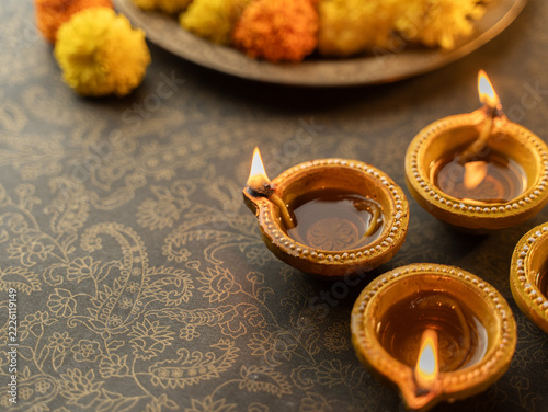 Four Traditional Clay Diwali Diyas with Flickering Flames Arranged on an Ornate Golden Patterned Surface, Warm Festive Close-Up Shot.