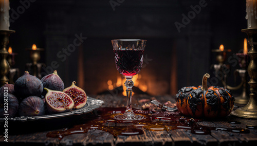 Gothic Halloween Feast with Red Wine in Crystal Goblet, Fresh Ripe Figs on Silver Platter, Charred Pumpkin, and Fireplace Glow
