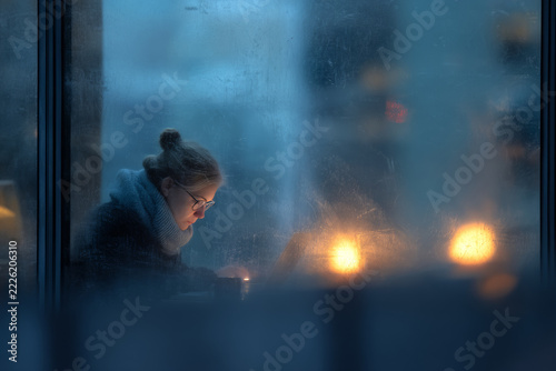 Young woman working on a laptop inside a cozy cafe during a cold winter evening