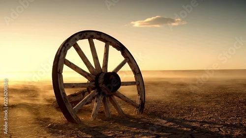 An old wooden wagon wheel abandoned in a barren desert landscape during a dusty sunset