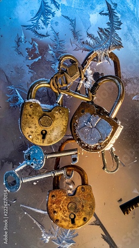 Weathered antique brass padlocks and skeleton keys covered in sparkling ice crystals and frost