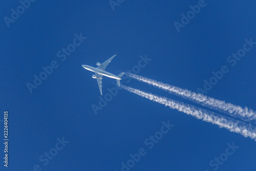 a white airplane flying in a clear, deep blue sky, leaving behind two distinct, white contrails