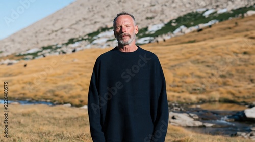 Portrait of mature man in black sweater standing in alpine meadow landscape for outdoor background and lifestyle banner
