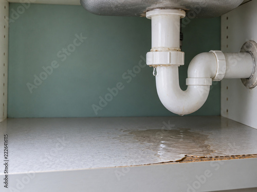 Leaking white plastic sink drain pipe causing water damage in cabinet