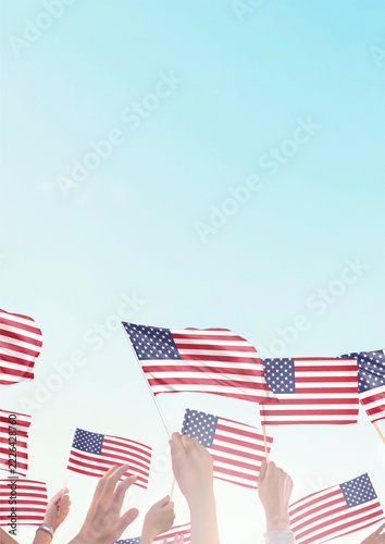 Hands waving American flags against a bright blue sky at a patriotic celebration