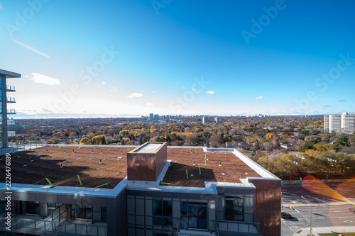 Photography Rooftop view from a modern apartment building over an autumn suburban cityscape with colorful fall trees and a distant downtown skyline under a clear blue sky