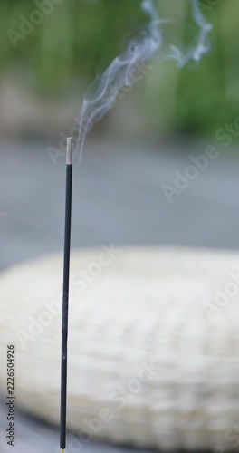Vertical video: Incense tip smoking, smoke splitting and drifting right over mat on patio by breeze
