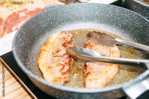 Obraz na plátně Pork chops searing in a frying pan with kitchen tongs