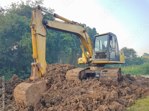 a yellow excavator resting on a pile of excavated dirt at an outdoor development site.