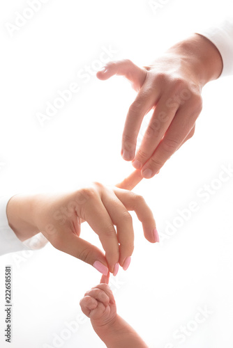 A father holds the mother’s hand, and the mother’s hand holds the infant’s hand, against a white background.