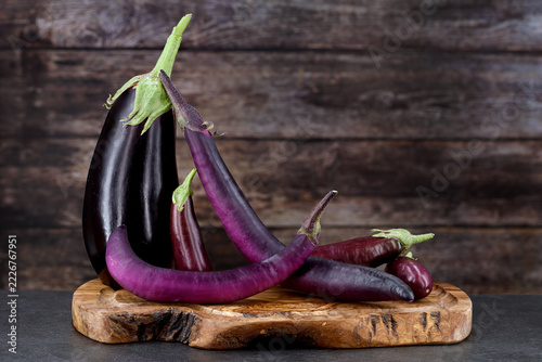 Different varieties of purple eggplant Solanum melongena arranged on a rustic wooden board