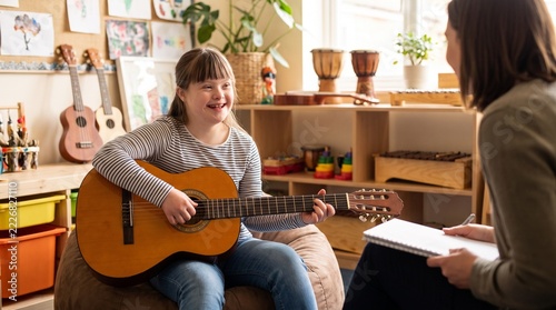 Young girl with Down syndrome learns to play the acoustic guitar while sitting on a beanbag chair