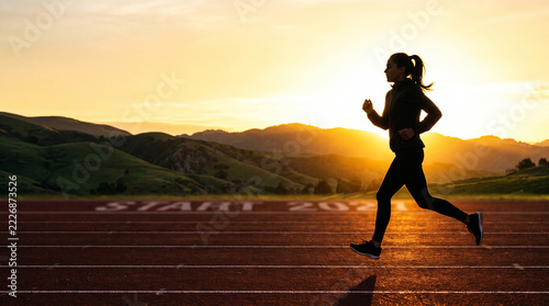 Silhouette of a female runner on a track with start 2027 text at sunrise