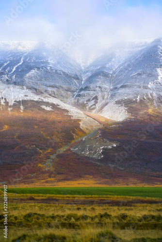 Scenic vertical landscape of majestic snow-capped mountain covered in clouds during autumn winter transition in Iceland. Majestic Nordic wilderness and nature background.