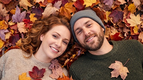 Smiling couple lying together on colorful fallen autumn maple leaves