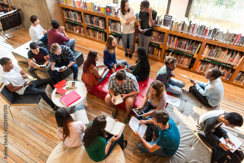 Diverse group of students studying in a library with books and tablets.