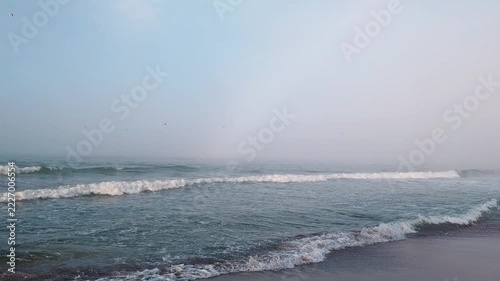 Foggy seaside with waves on sand coast, moody sea atmosphere