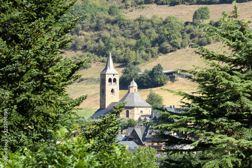 Scenic look at the old stone church tower of Vilac village peaking behind pine tree foliage on a sunny day. Aran Valley, Spain.