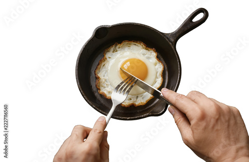Person cutting fried egg in a cast iron skillet isolated on black background