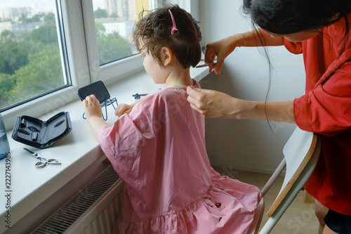 Mother trimming her son's hair neckline at home.