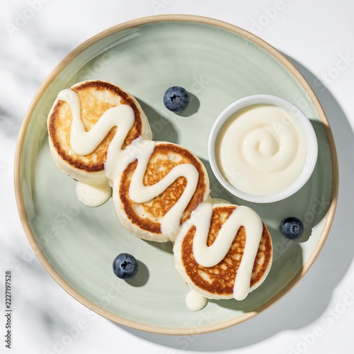 Three thick syrniki arranged diagonally on a ceramic plate with fresh blueberries and sweet topping — high key lighting food background for homemade dessert and traditional dish