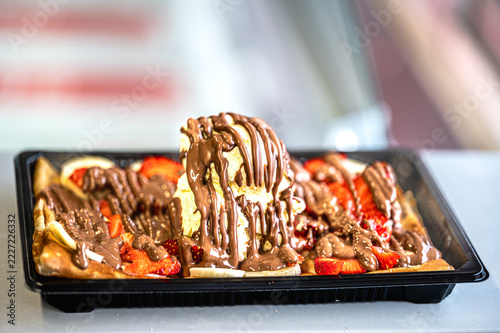 Freshly baked crepe and waffel with ice cream, chocolate and berries on wooden table. Served with spoon. Filled pancakes with strawberries, fresh berries and sauce.