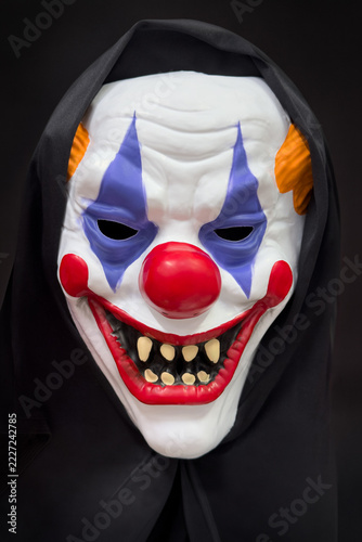 Creepy clown mask with sharp teeth and painted eyes on a black background, halloween