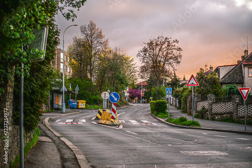 European suburban road junction with traffic signs, speed bumps, and green spring trees at sunset