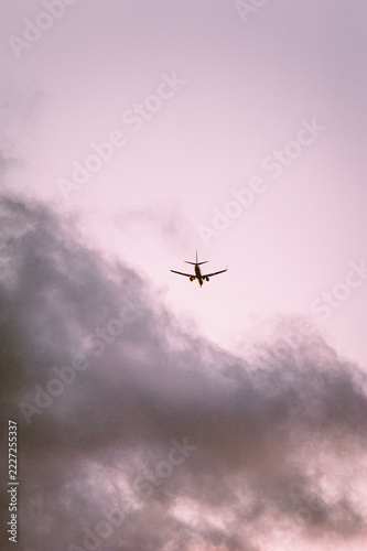 Silhouette of a commercial airplane flying through soft pink sunset clouds in the sky