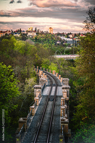 Old stone railway viaduct stretching over a lush green valley toward distant city buildings at twilight