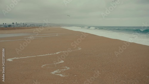Wide sandy beach extends toward the Pacific Ocean beneath gray skies during unsettled weather.