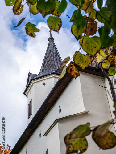 Autumn Church Steeple Framed by Golden Leaves Against a Cloudy Blue Sky