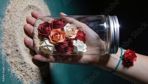Hand holding glass jar filled with small red roses on sand background