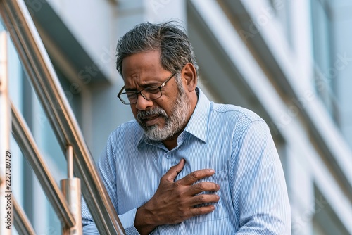 Elderly man experiencing chest pain while holding his hand over his heart on outdoor stairs