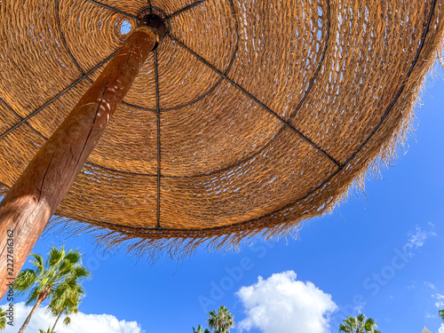 Low angle view of a straw beach umbrella against a blue sky