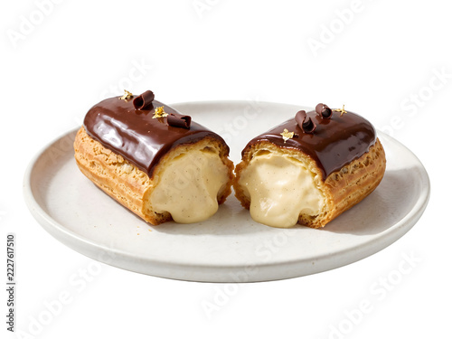 Chocolate eclair sliced in half showing creamy vanilla custard filling on a transparent background ceramic plate against a transparent background.