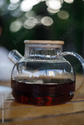 Close-up of a glass teapot filled with dark tea on a wooden table with bokeh background