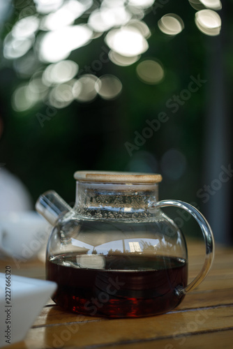 Glass Teapot with Dark Tea on Wooden Table with Bokeh Background