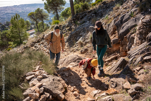 Family hiking together on rocky mountain trail, senior man, young woman and small child exploring nature, outdoor adventure, active lifestyle, multigenerational bonding, freedom
