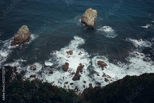 Aerial view of Atlantic Ocean waves crashing around rocky sea stacks below dramatic cliffs on the northern coast of Spain.