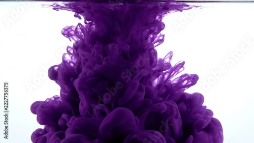 Deep purple ink cloud dissolving in clear water slowly swirling down forming abstract smoky shapes against white background isolated footage.