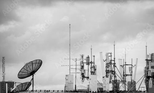 Modern 5G telecommunication equipment with cellular antennas and satellite dishes on a city rooftop during cloudy daylight. Wireless internet, broadcasting, data transmission and network coverage.