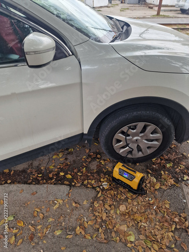 A pump is inflating a tire on a car parked on the street.