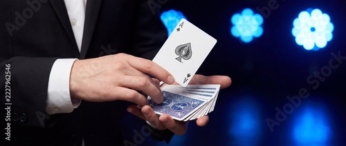 Magician displaying ace of spades playing card above a deck on stage. Close-up of card handling during a magic trick. Entertainment and illusion. Casino games and sleight of hand.