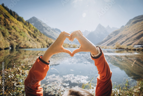 Obraz na plátně Hands forming a heart shape frame a serene mountain lake and sunlit peaks in Dom
