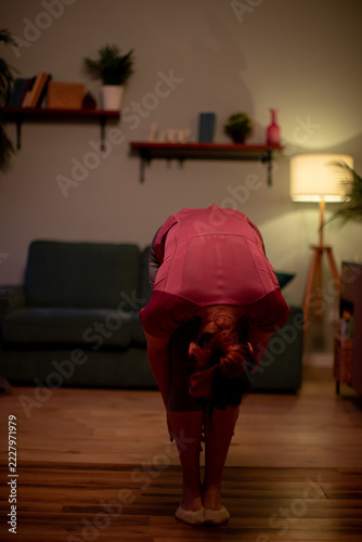 Gentle stretch at home. Maintaining comfort with calming evening stretch routine. Engaging in soothing selfcare stretch on wooden flooring by sofa in warm light